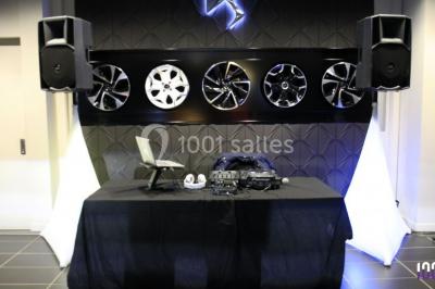 Salle de réception éclairée avec des lumières colorées, vue depuis une table de DJ équipée d'un ordinateur et de platines.