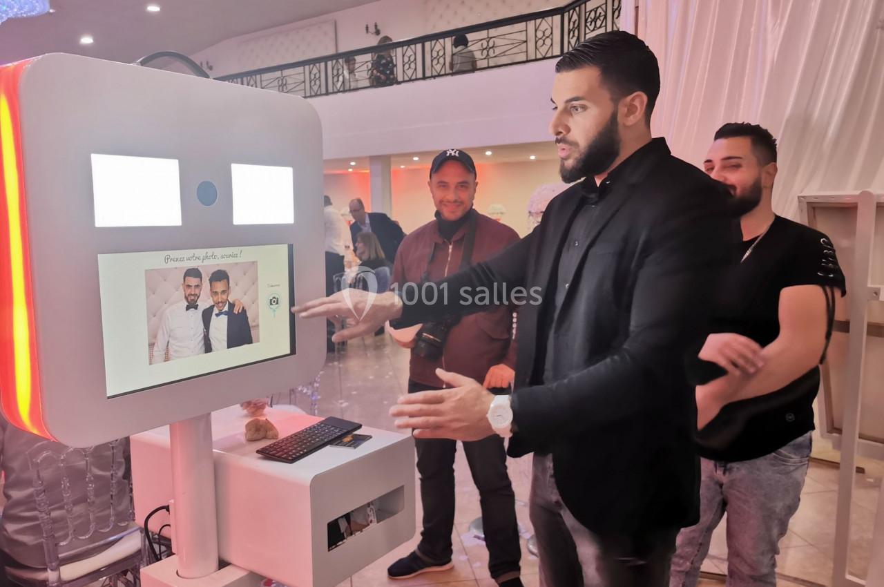 Un homme interagit avec une borne photo dans un espace intérieur lumineux, entouré de plusieurs personnes.
