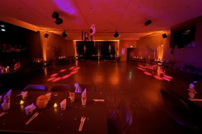 Salle de réception éclairée avec des lumières colorées, vue depuis une table de DJ équipée d'un ordinateur et de platines.