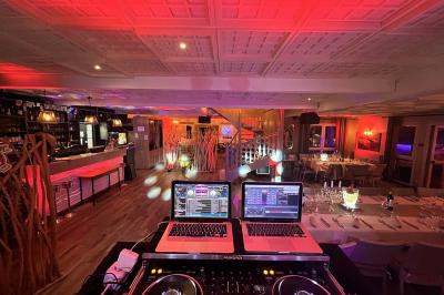 Salle de réception éclairée avec des lumières colorées, vue depuis une table de DJ équipée d'un ordinateur et de platines.