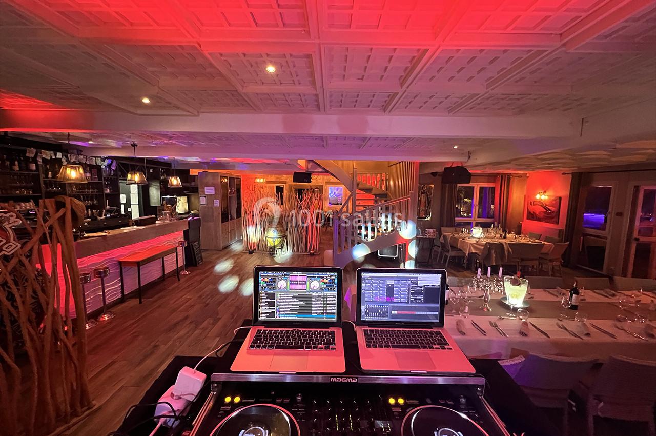 Vue depuis une table de mixage sur une salle de réception éclairée de lumières rouges et décorée pour un événement.