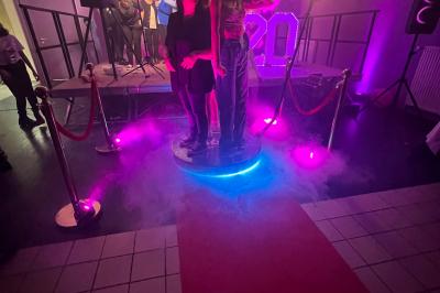 Salle de réception éclairée avec des lumières colorées, vue depuis une table de DJ équipée d'un ordinateur et de platines.