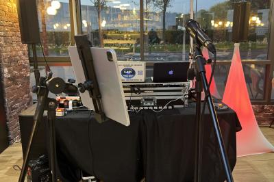 Salle de réception éclairée avec des lumières colorées, vue depuis une table de DJ équipée d'un ordinateur et de platines.