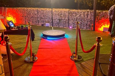 Salle de réception éclairée avec des lumières colorées, vue depuis une table de DJ équipée d'un ordinateur et de platines.
