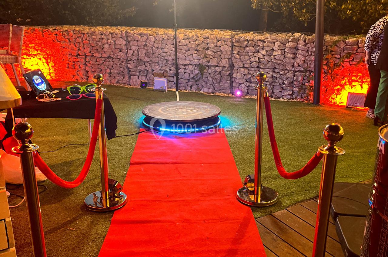 Tapis rouge menant à une plateforme circulaire éclairée, entourée de poteaux dorés et d'une lumière annulaire en extérieur.