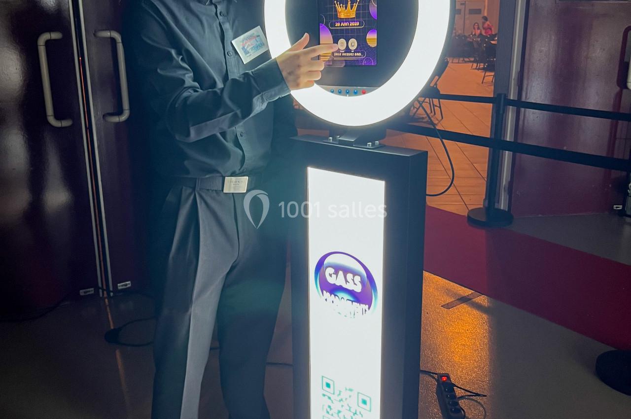 Un homme en chemise sombre utilise une borne photo équipée d'un anneau lumineux et d'un écran tactile.
