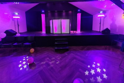 Scène éclairée de lumières violettes avec une piste de danse en parquet et des ballons au sol.