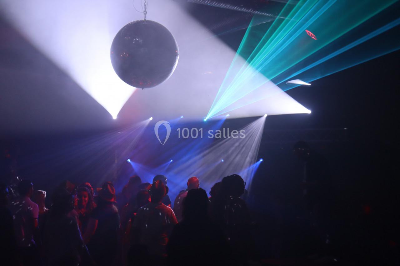 Personnes dansant sous une boule disco avec des faisceaux lumineux colorés dans une ambiance sombre.