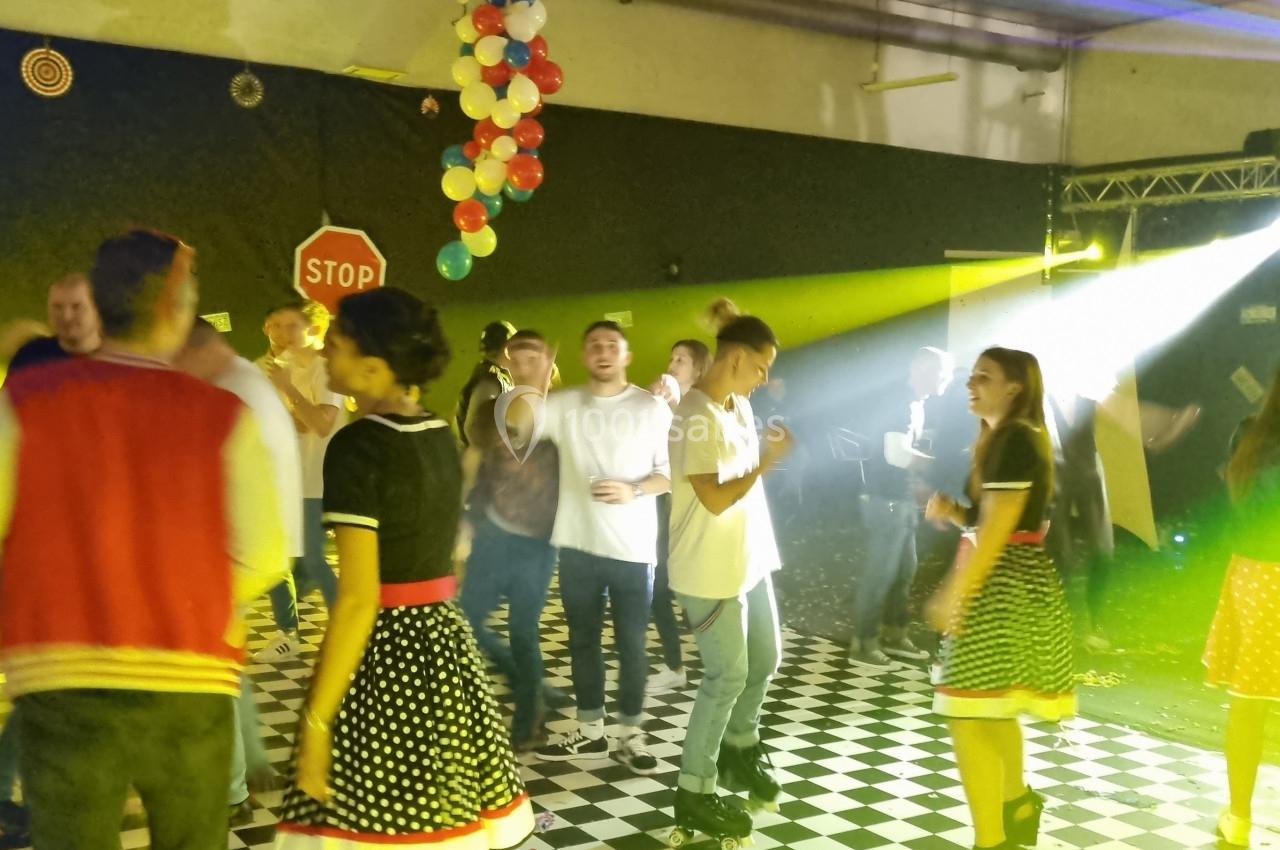 Des personnes dansent sur une piste éclairée par des jeux de lumière, décorée de ballons et d'éléments rétro.