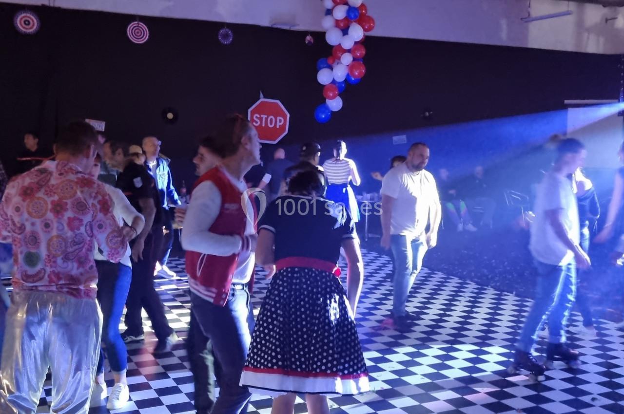 Des personnes dansent sur une piste à damier, éclairée par des projecteurs, avec des décorations suspendues.