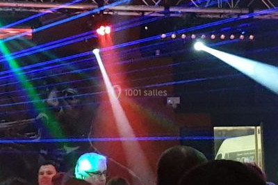 Vue depuis une table de mixage sur une salle éclairée par des lumières colorées, avec des invités assis et debout.