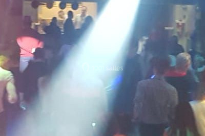 Vue depuis une table de mixage sur une salle éclairée par des lumières colorées, avec des invités assis et debout.