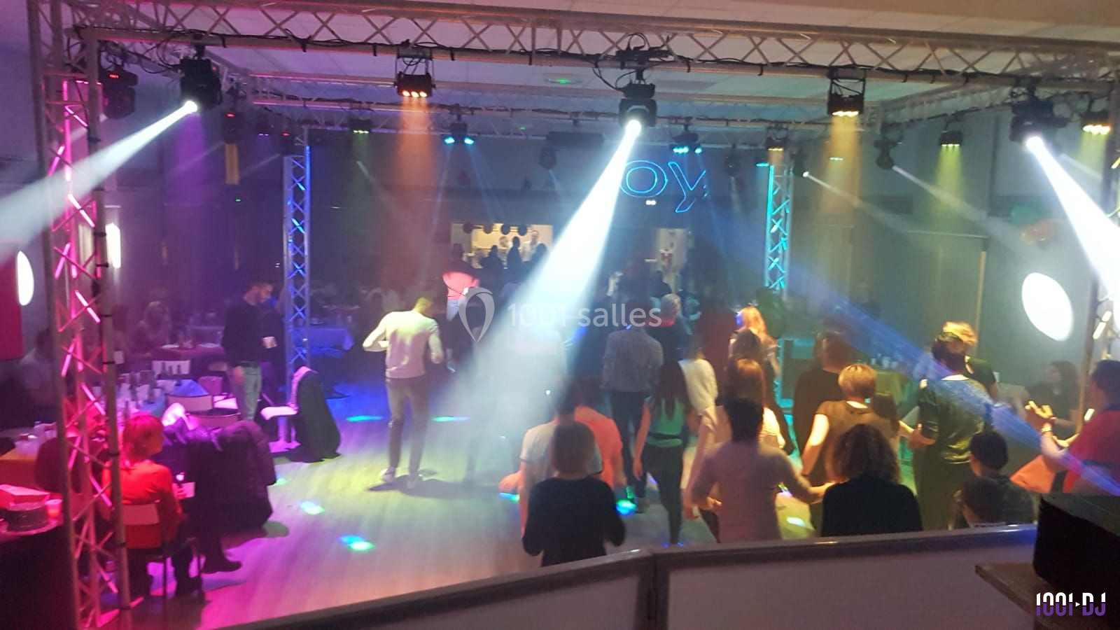 Des personnes dansent sur une piste éclairée par des jeux de lumière colorés dans une salle animée.