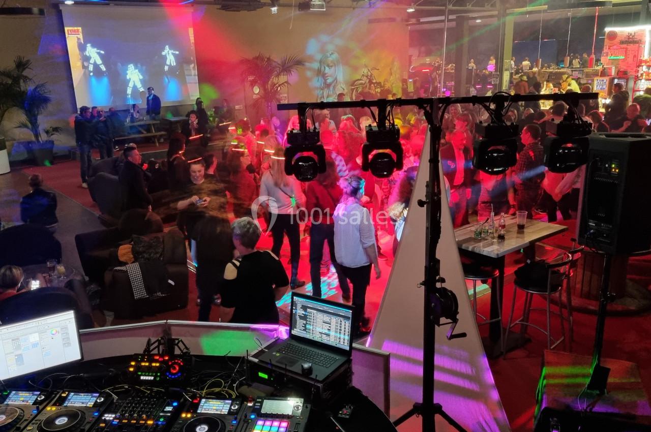 Vue d'une soirée animée avec des personnes dansant sous des jeux de lumière colorés, vue depuis une table de DJ.