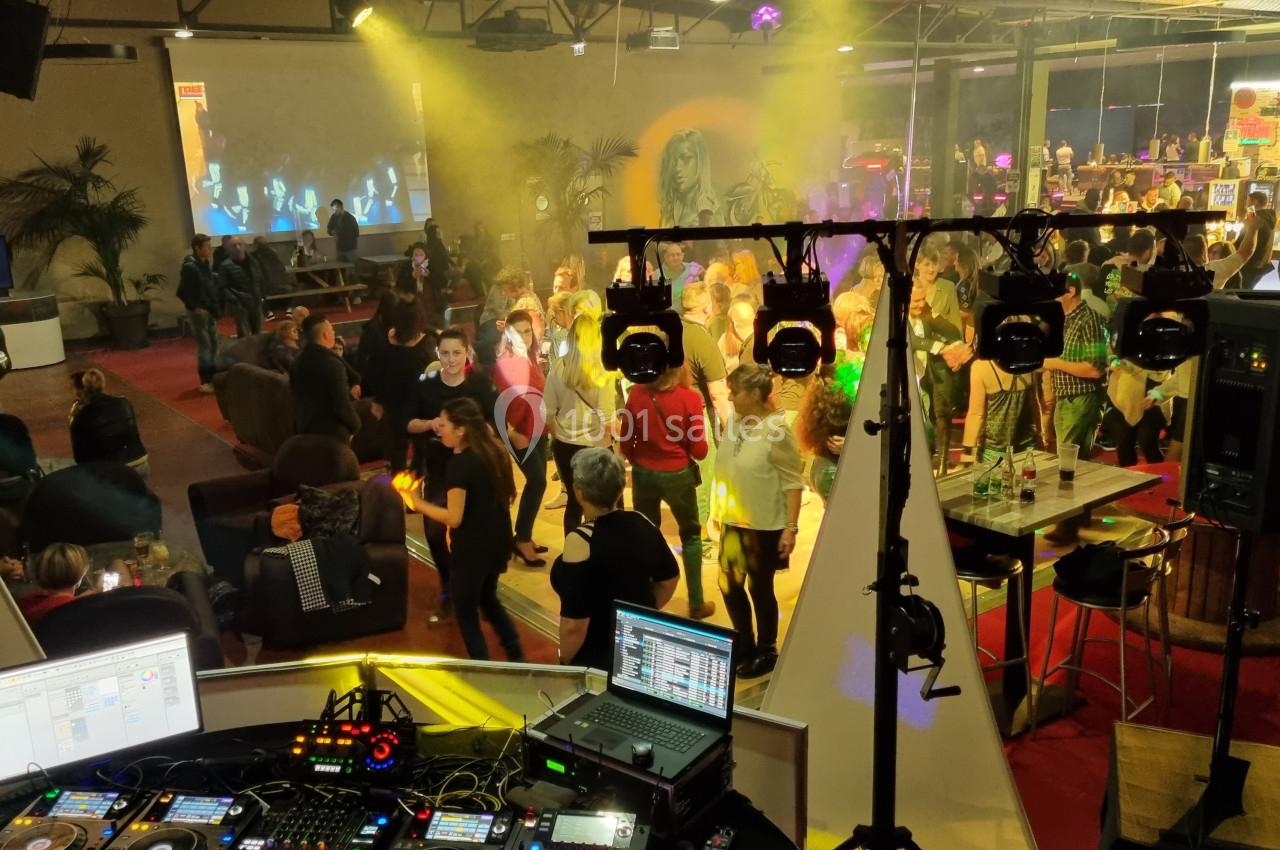 Vue d'une soirée animée avec des personnes dansant sur une piste éclairée, observée depuis une cabine de DJ.