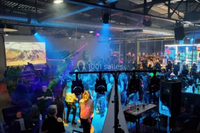 Vue depuis une table de mixage sur une salle éclairée par des lumières colorées, avec des invités assis et debout.