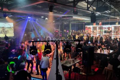 Vue depuis une table de mixage sur une salle éclairée par des lumières colorées, avec des invités assis et debout.