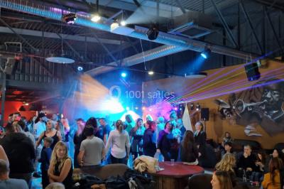 Vue depuis une table de mixage sur une salle éclairée par des lumières colorées, avec des invités assis et debout.