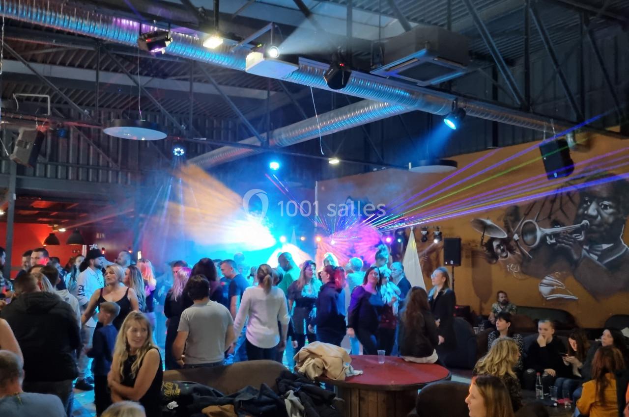 Groupe de personnes dans une salle animée avec jeux de lumière colorés et fresque murale représentant un trompettiste.