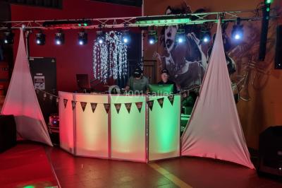 Vue depuis une table de mixage sur une salle éclairée par des lumières colorées, avec des invités assis et debout.