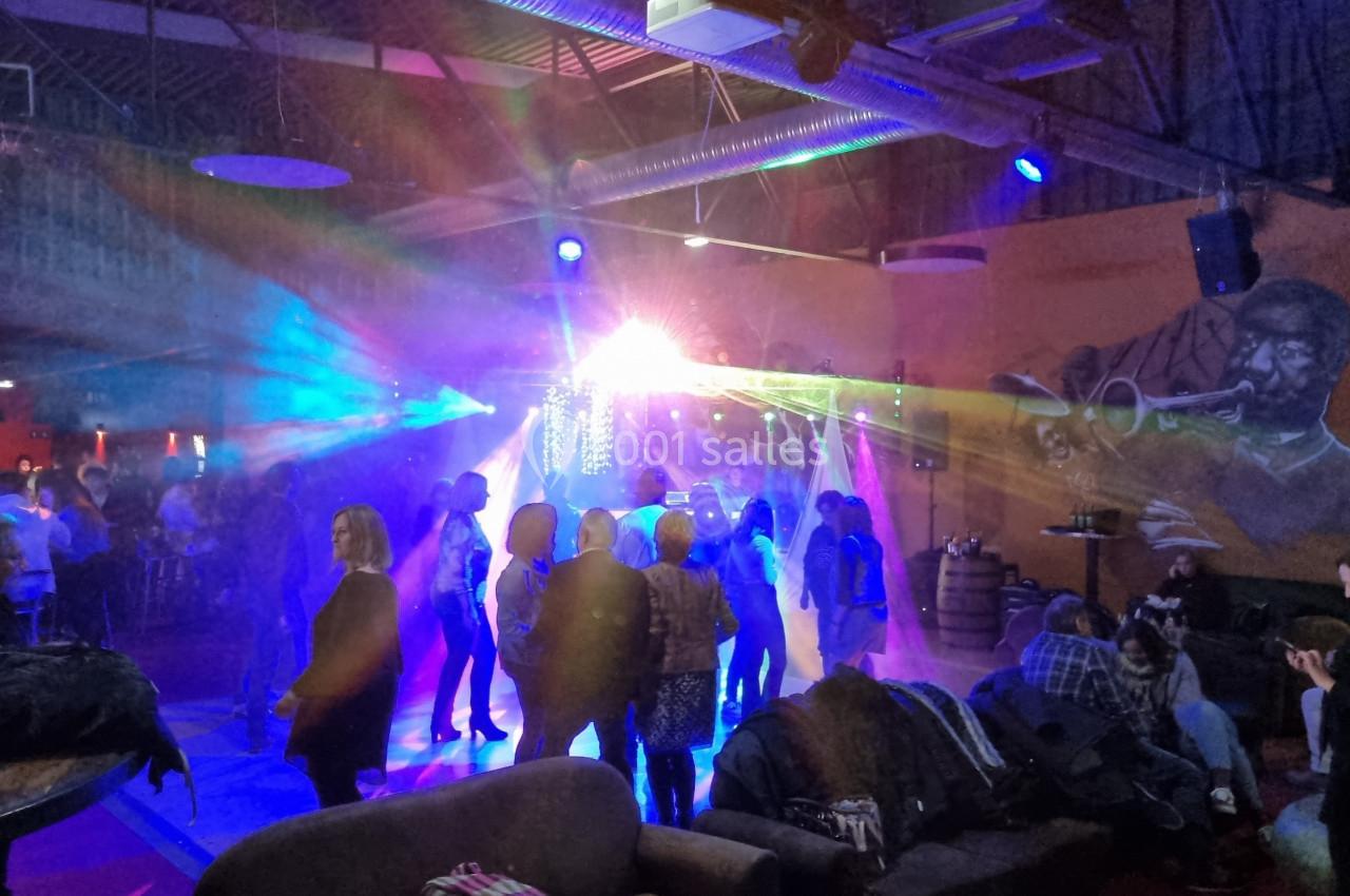 Groupe de personnes dans une salle animée avec jeux de lumière colorés et fresque murale représentant un musicien.