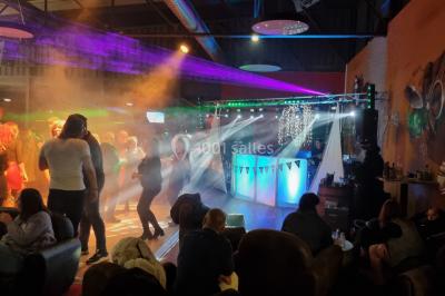 Vue depuis une table de mixage sur une salle éclairée par des lumières colorées, avec des invités assis et debout.