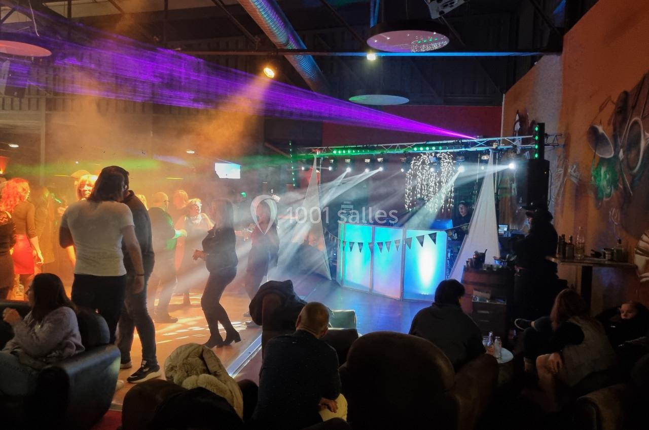 Personnes dansant sur une piste éclairée par des jeux de lumière colorés, avec un DJ en arrière-plan.