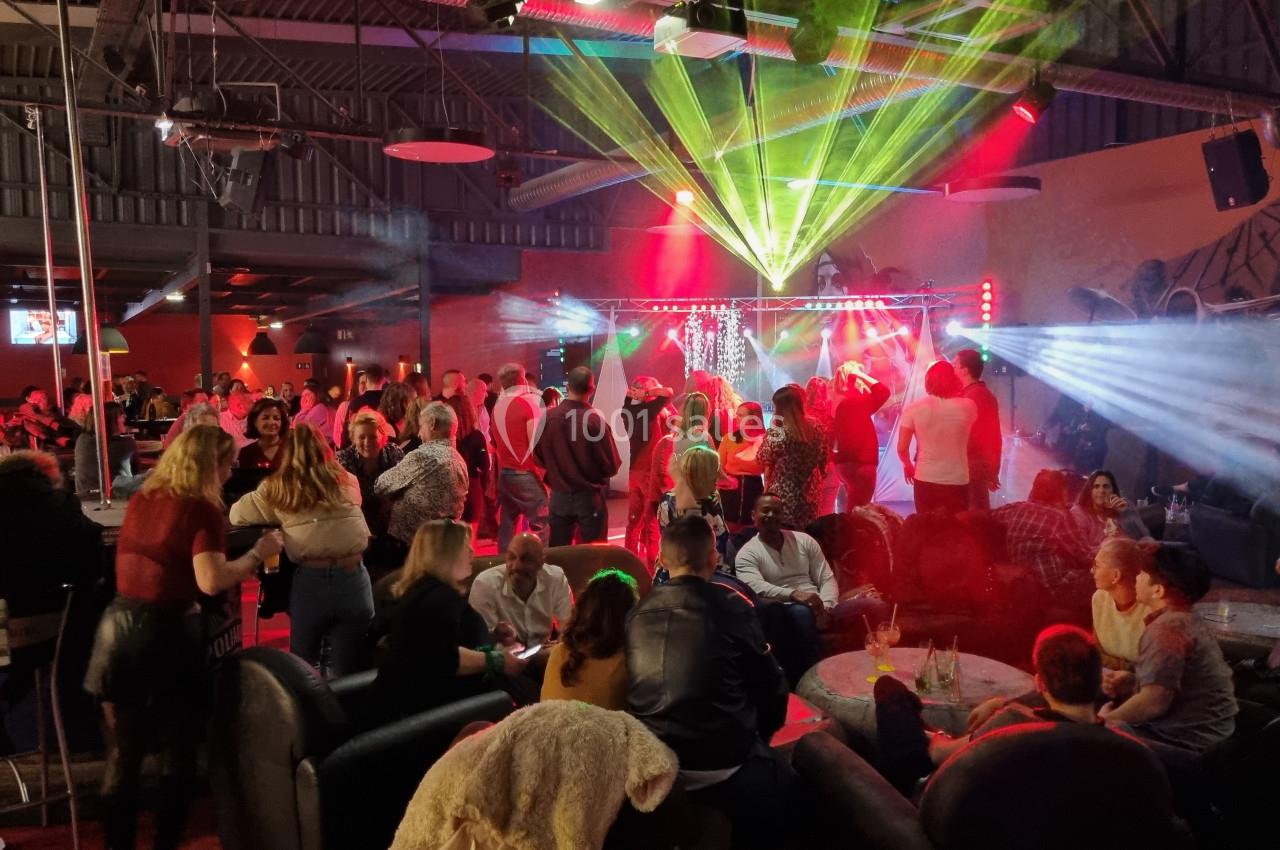 Groupe de personnes dans un bar ou club, éclairé par des lumières colorées, avec une scène en arrière-plan.