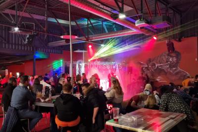 Vue depuis une table de mixage sur une salle éclairée par des lumières colorées, avec des invités assis et debout.