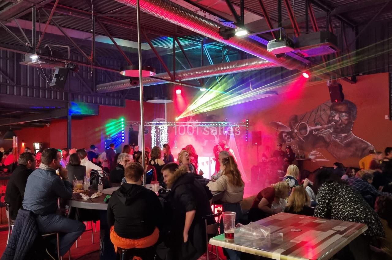Salle animée avec des tables occupées, un spectacle sur scène éclairé par des lumières colorées et un mur décoré d'une…