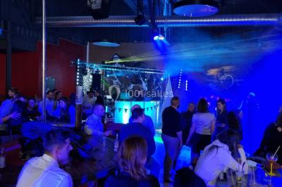 Vue depuis une table de mixage sur une salle éclairée par des lumières colorées, avec des invités assis et debout.