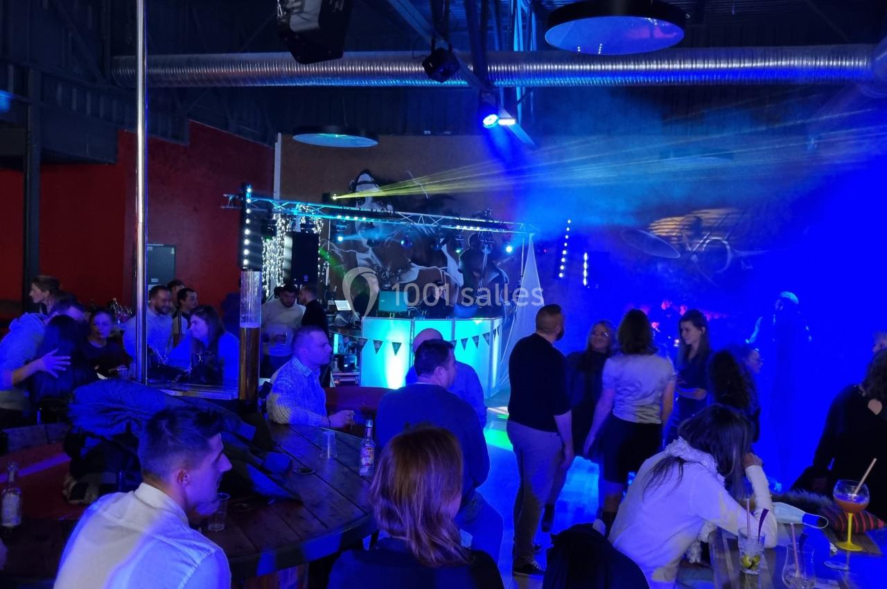 Des personnes dansent et discutent dans une salle avec éclairage coloré, musique et ambiance festive.