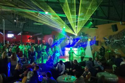 Vue depuis une table de mixage sur une salle éclairée par des lumières colorées, avec des invités assis et debout.