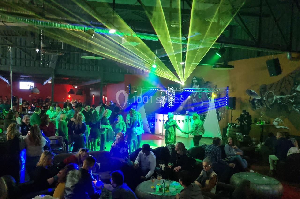 Salle animée avec des jeux de lumières colorées, des personnes discutant et dansant dans une ambiance festive.