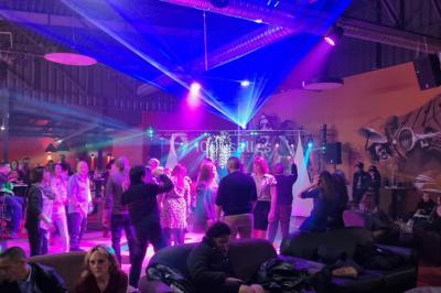 Vue depuis une table de mixage sur une salle éclairée par des lumières colorées, avec des invités assis et debout.