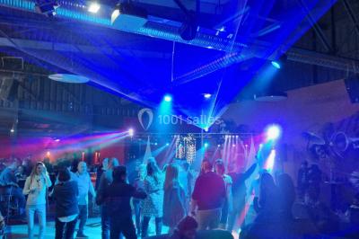 Vue depuis une table de mixage sur une salle éclairée par des lumières colorées, avec des invités assis et debout.