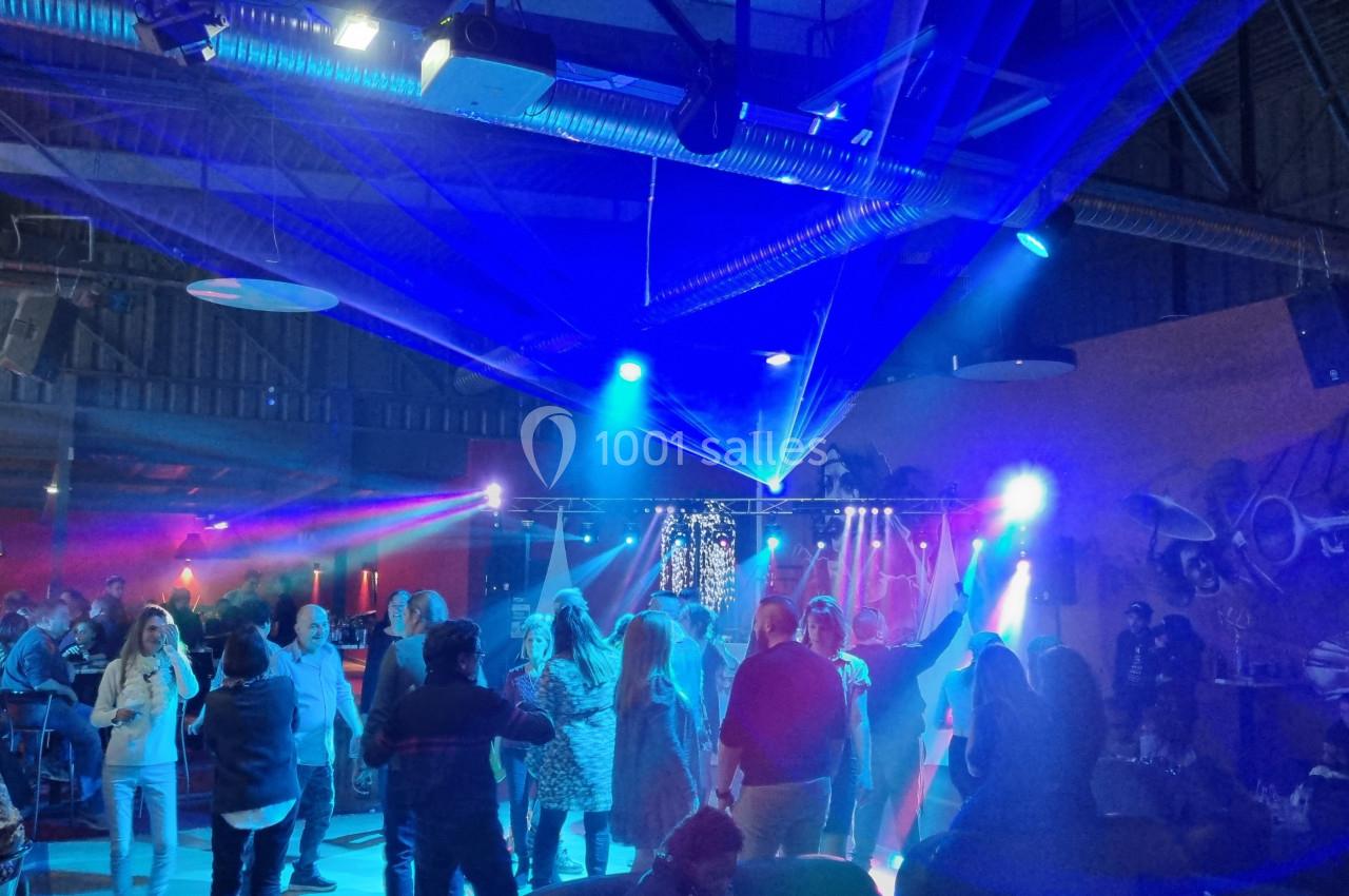 Des personnes dansent sous des lumières colorées dans une salle avec un plafond industriel et des projecteurs.