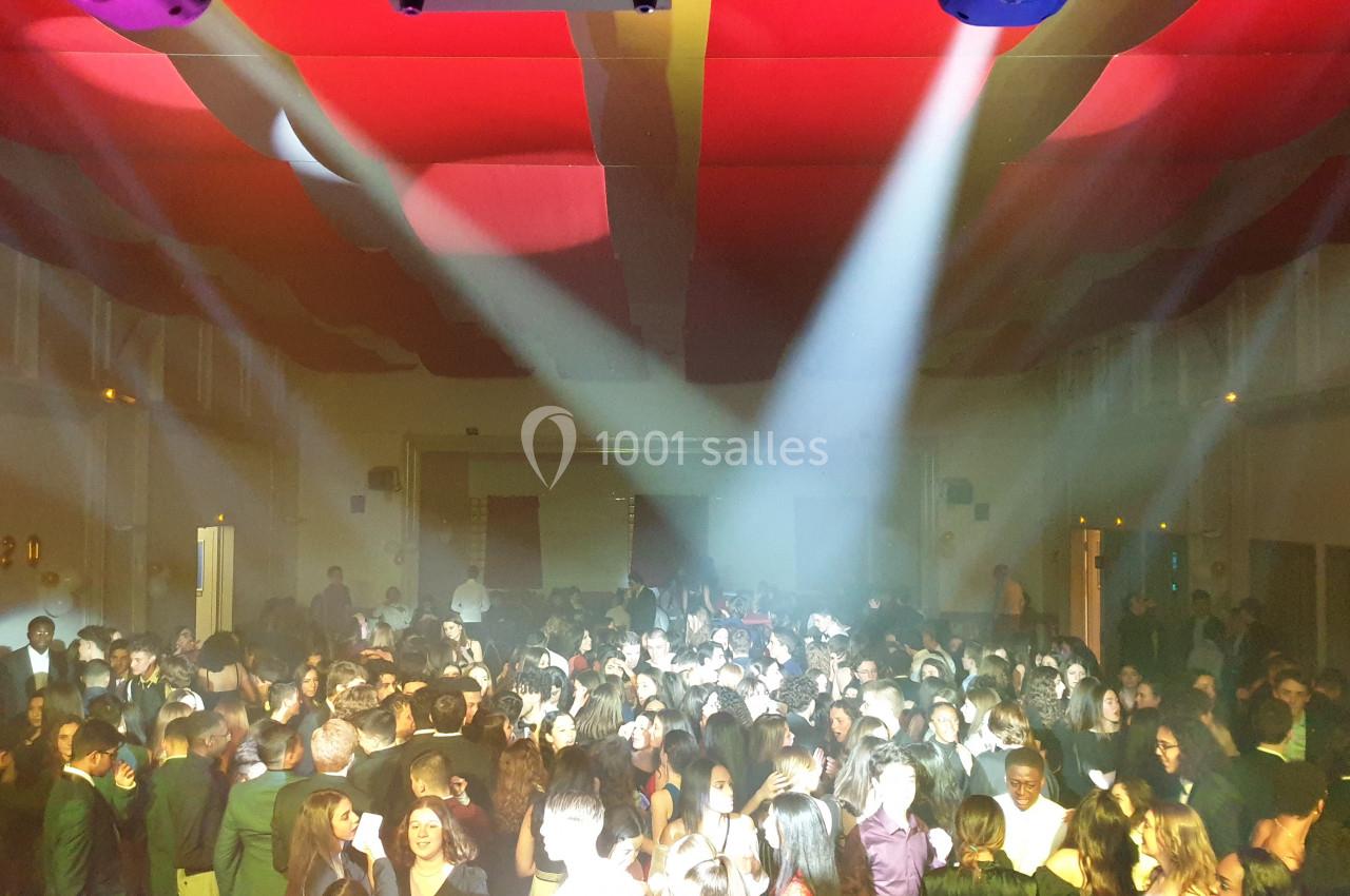 Salle comble avec des personnes dansant sous des éclairages colorés et un plafond décoré de tissus rouges.