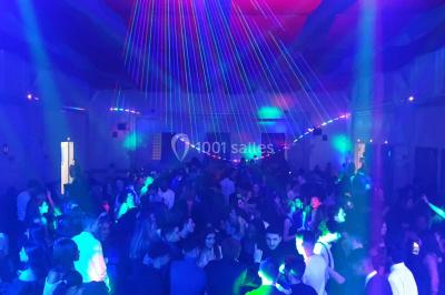 Vue depuis une table de mixage sur une salle éclairée par des lumières colorées, avec des invités assis et debout.