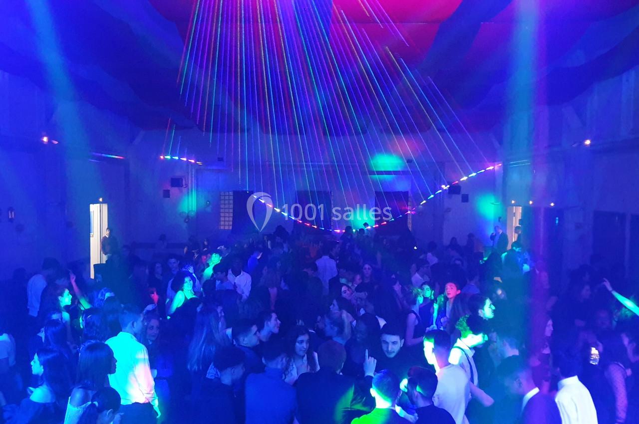 Foule dans une salle illuminée par des jeux de lumière colorés lors d'une soirée festive.