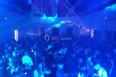 Vue depuis une table de mixage sur une salle éclairée par des lumières colorées, avec des invités assis et debout.