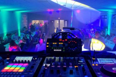 Vue depuis une table de mixage sur une salle éclairée par des lumières colorées, avec des invités assis et debout.