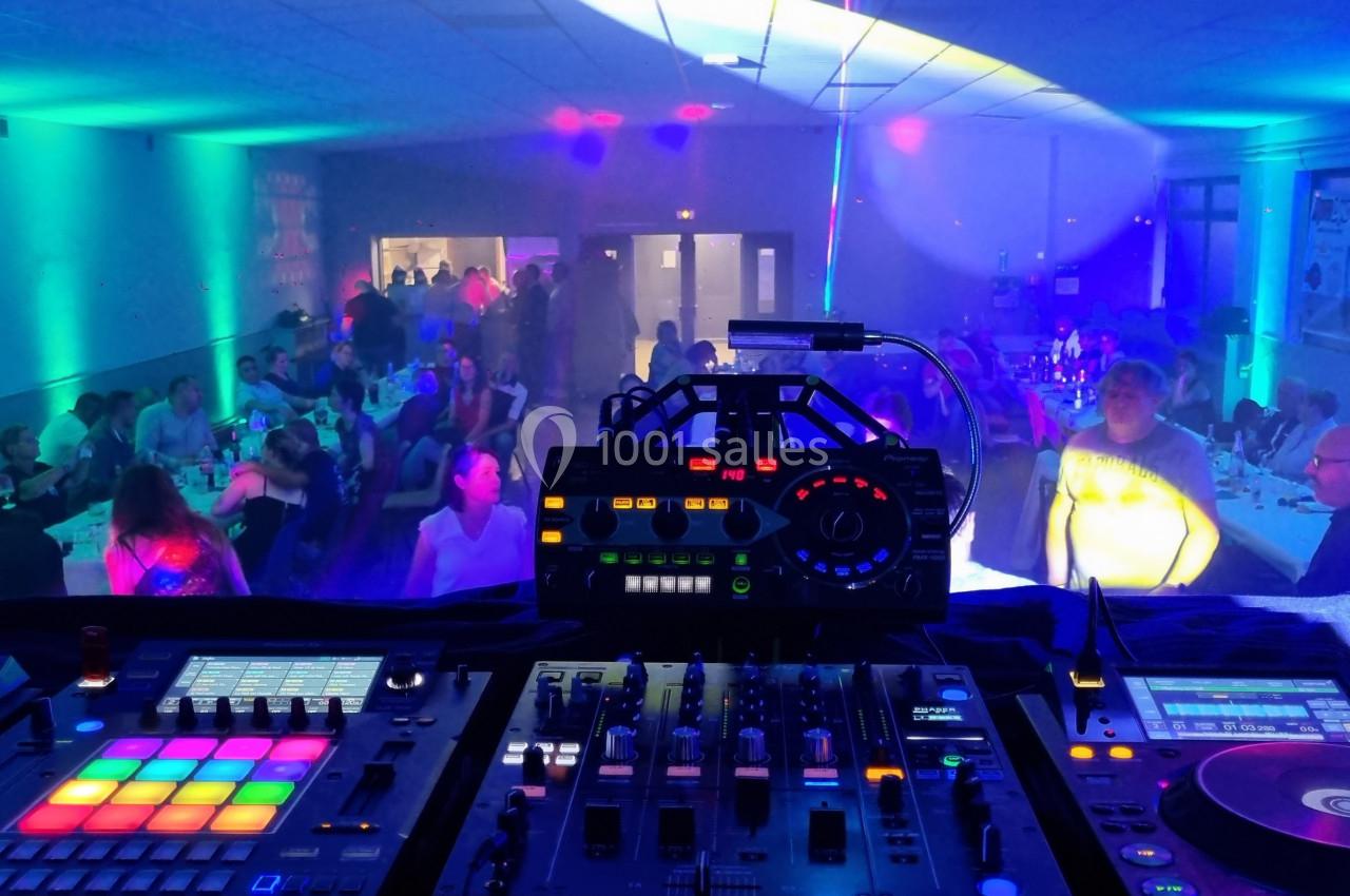 Vue depuis une table de mixage sur une salle éclairée par des lumières colorées, avec des invités assis et debout.