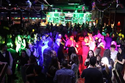Vue depuis une table de mixage sur une salle éclairée par des lumières colorées, avec des invités assis et debout.