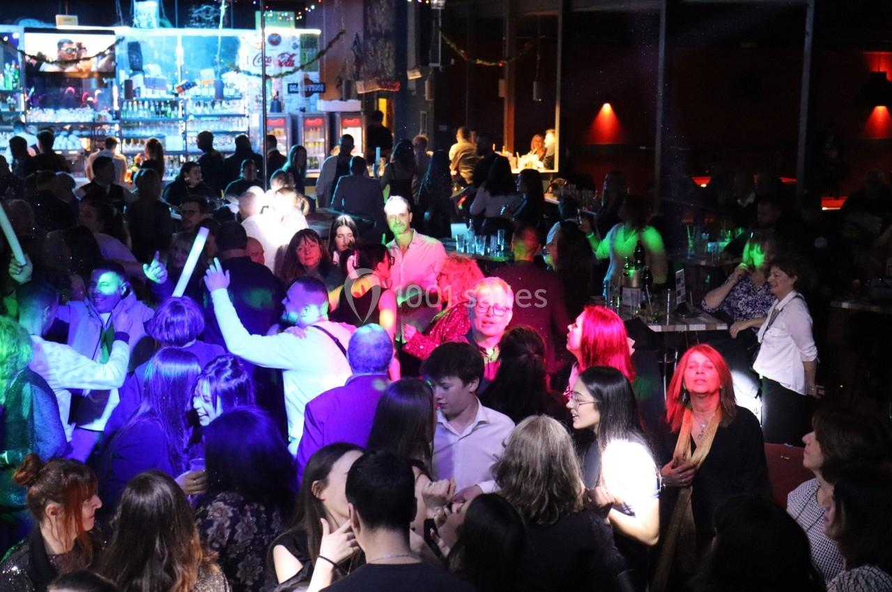 Groupe de personnes dans une ambiance festive avec éclairages colorés, dans un bar ou une salle animée.