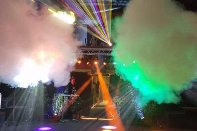 Vue depuis une table de mixage sur une salle éclairée par des lumières colorées, avec des invités assis et debout.