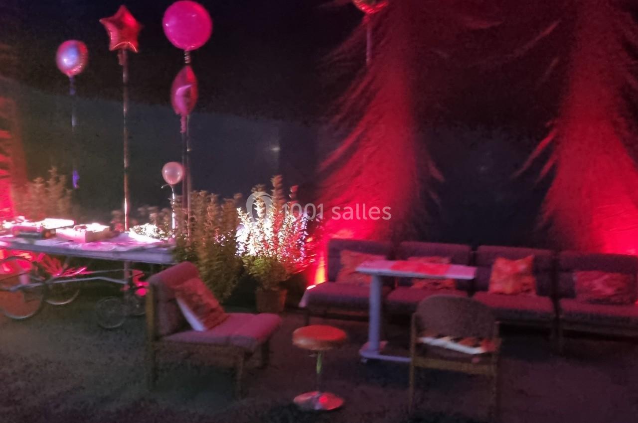 Espace lounge décoré avec des ballons, des canapés et un éclairage rouge dans une ambiance festive.