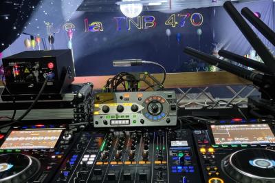 Vue depuis une table de mixage sur une salle éclairée par des lumières colorées, avec des invités assis et debout.