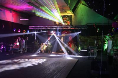 Vue depuis une table de mixage sur une salle éclairée par des lumières colorées, avec des invités assis et debout.