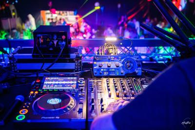 Vue depuis une table de mixage sur une salle éclairée par des lumières colorées, avec des invités assis et debout.